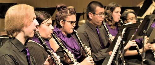 Six students wearing black and purple playing clarinets.