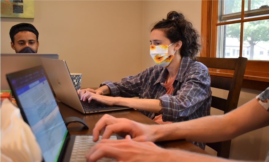 Three students, wearing masks, working with laptops
