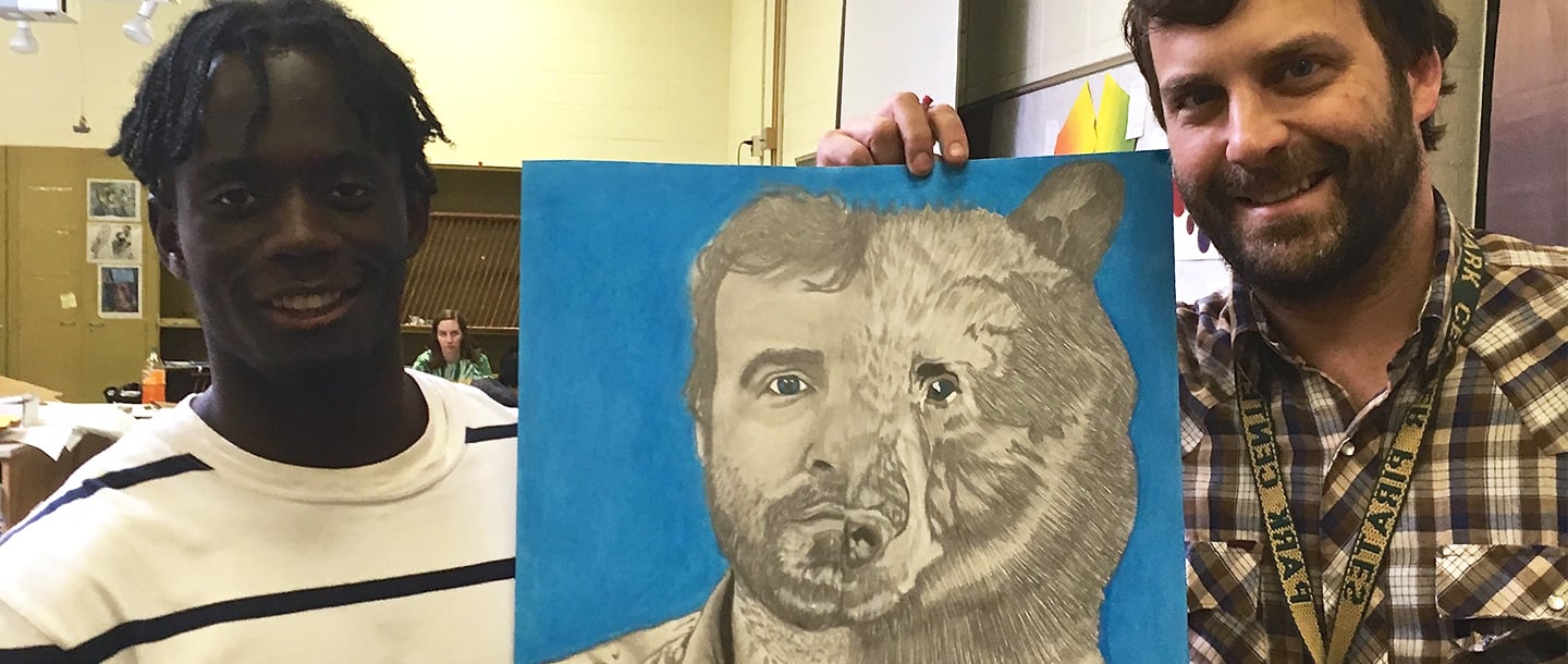 Art student with a collage painting of himself and a grizzly bear holding it with another student