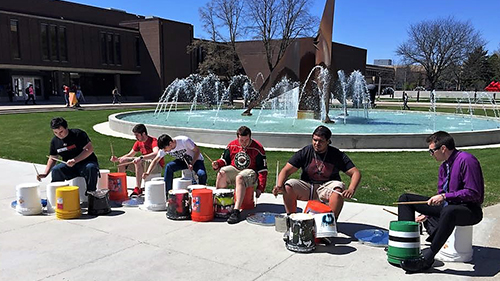 a group of people playing drums outside by a fountain